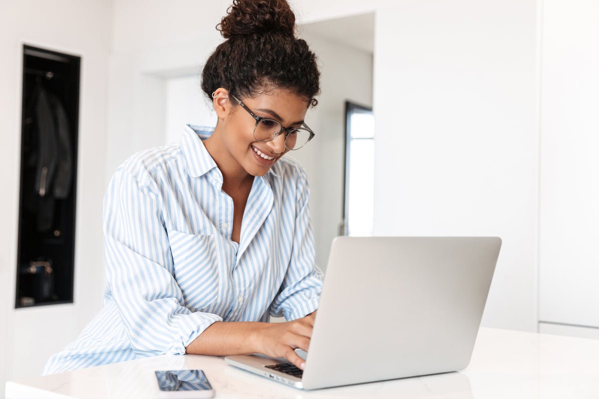young adult woman smiling and working on a laptop in a bright white space